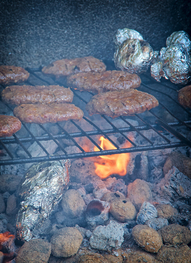 Spicy burger paties on a grill rack above glowing coals
