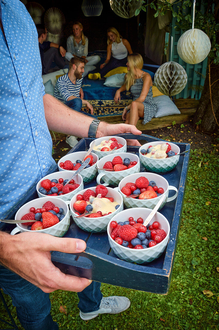 A man holding a tray of fresh berries and ice-cold sabayon