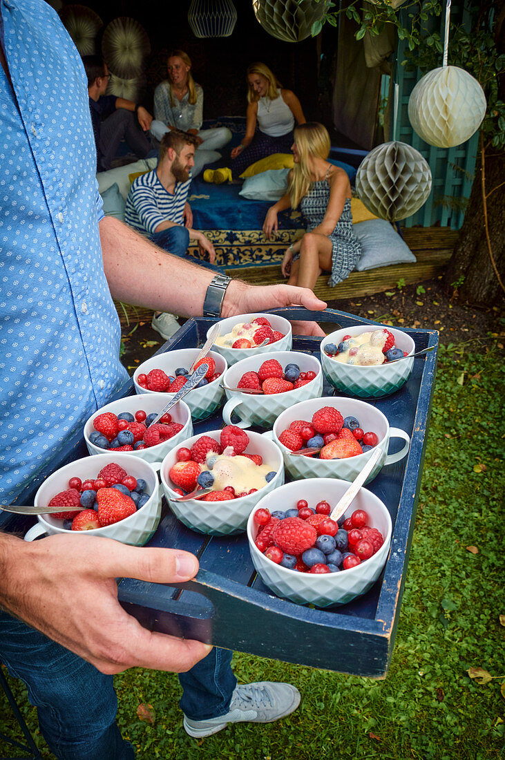 Mann hält Tablett mit frischen Beeren und eiskalter Zabaione