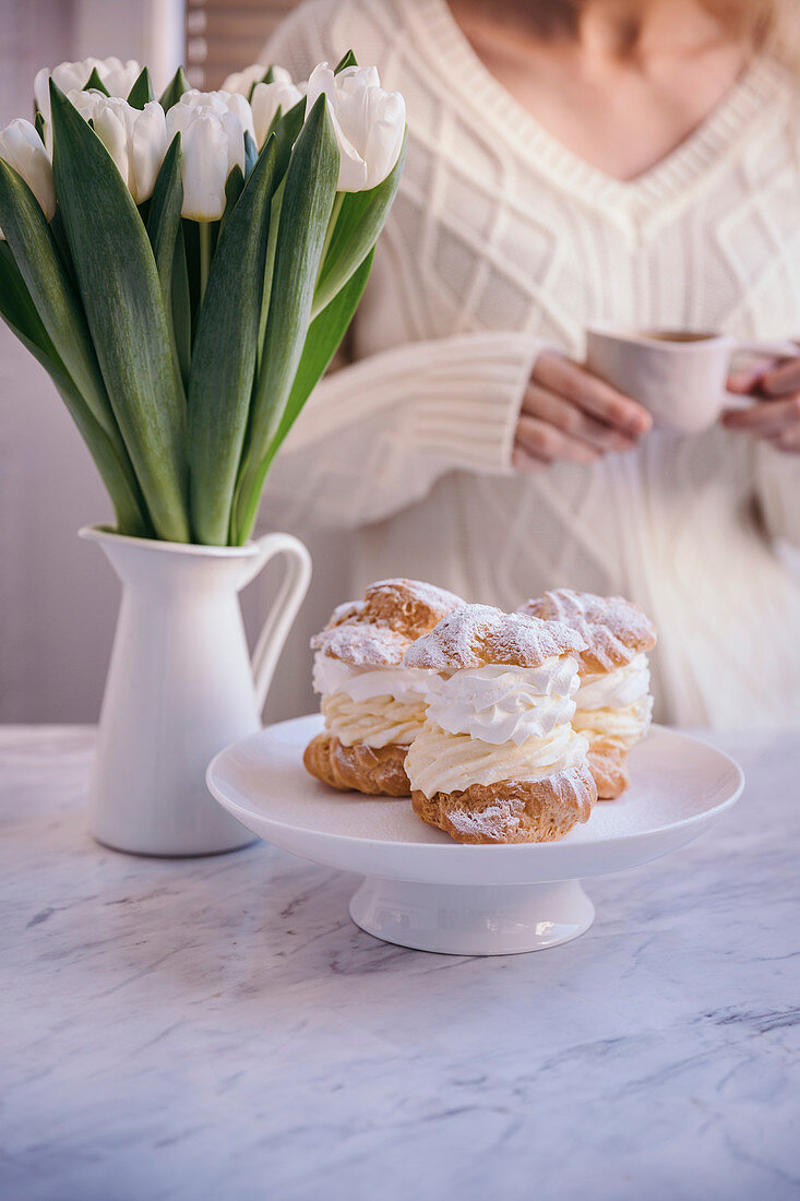 Woman drinking coffee and eating cream puff dessert