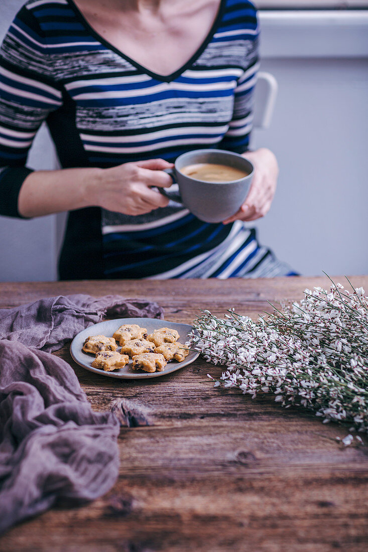 Frau mit einer Tasse Kaffee und Plätzchenteller an rustikalem Holztisch