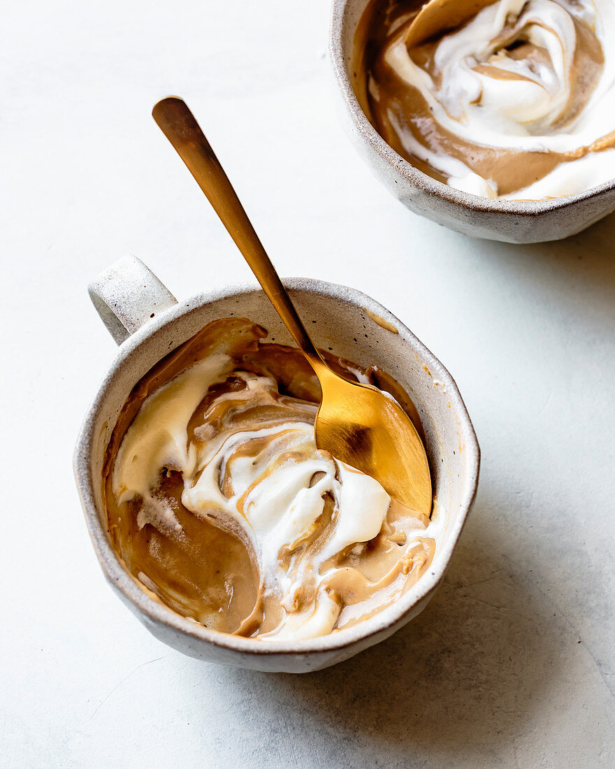 A butterscotch pudding in a cup, topped with cream
