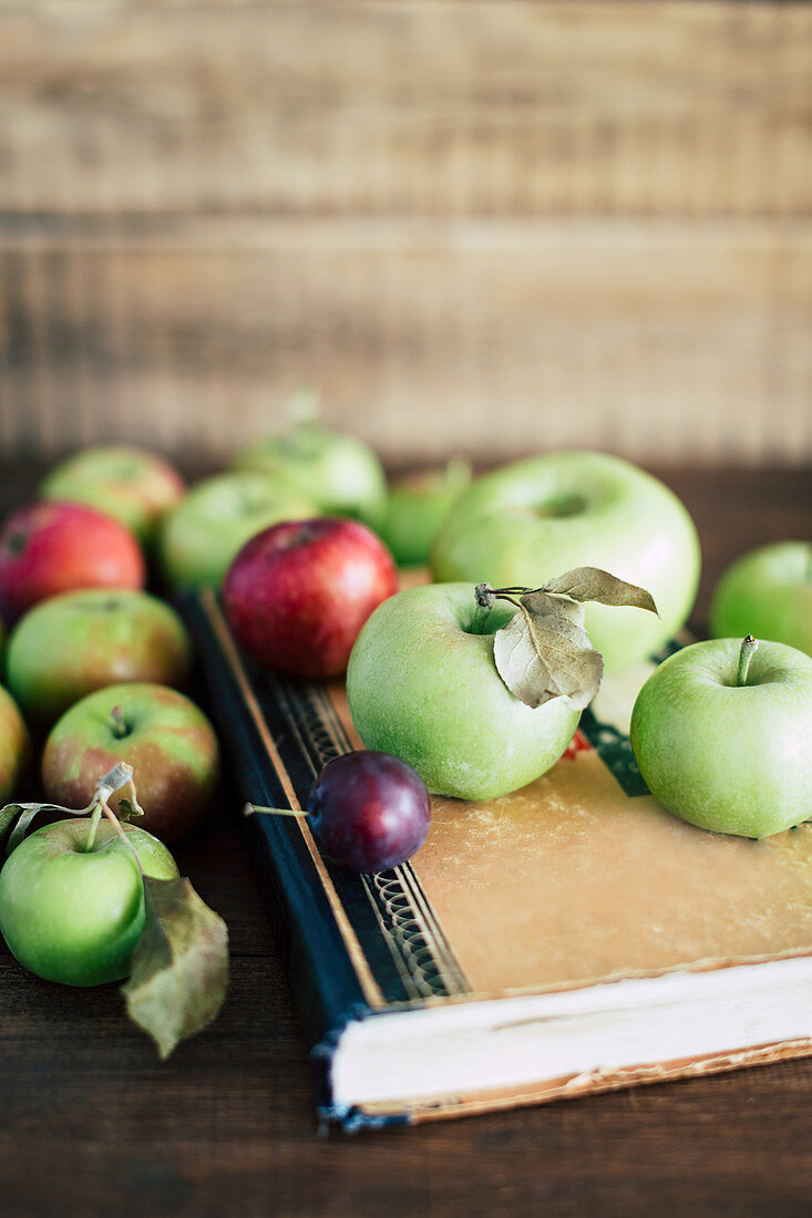 Bunch of ripe apples and small plum lying on shabby old book