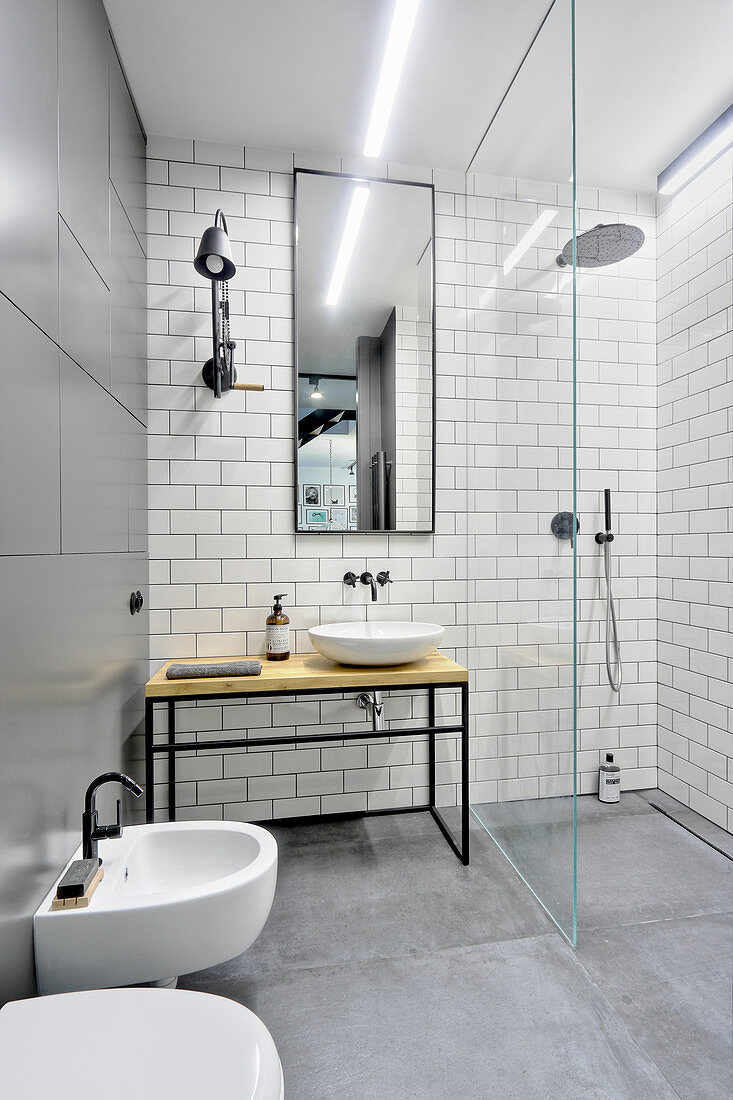 Industrial-style bathroom with metal and tiled walls and shower area behind glass partition