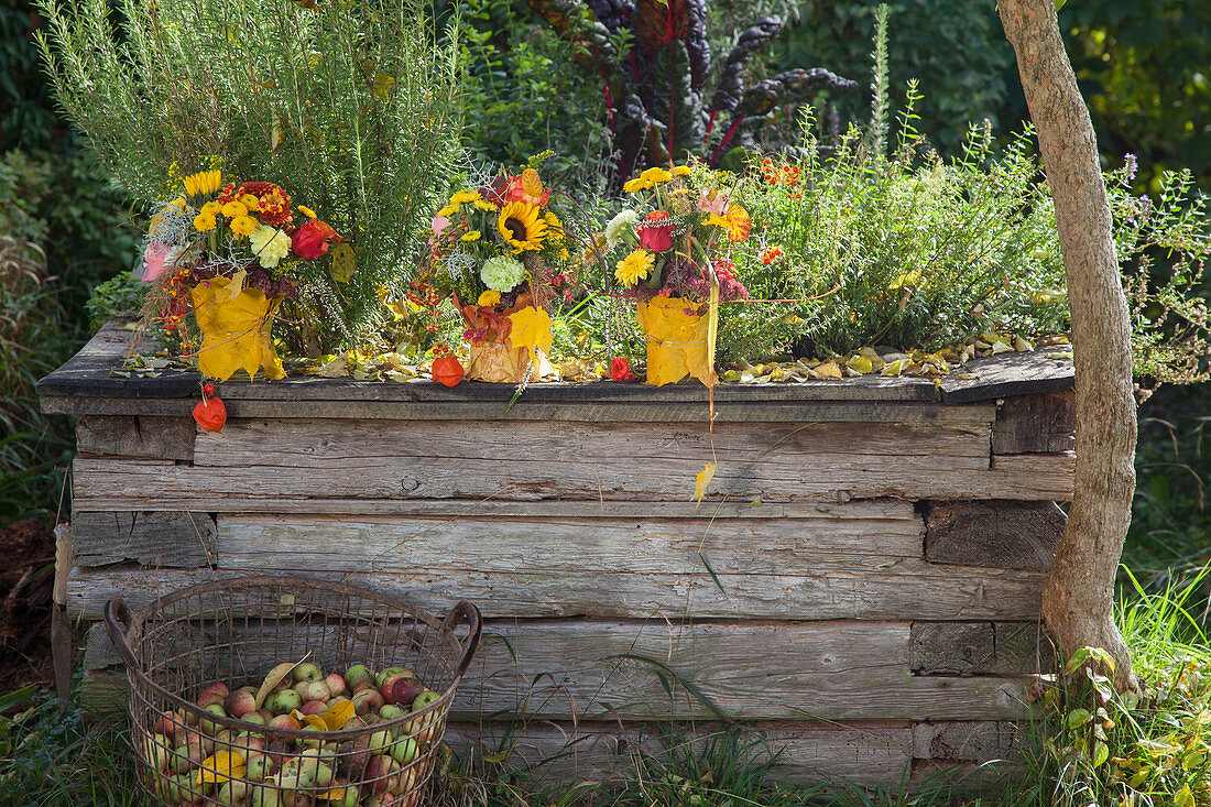 Bouquets of sunflowers and chrysanthemums in vases covered in autumn leaves