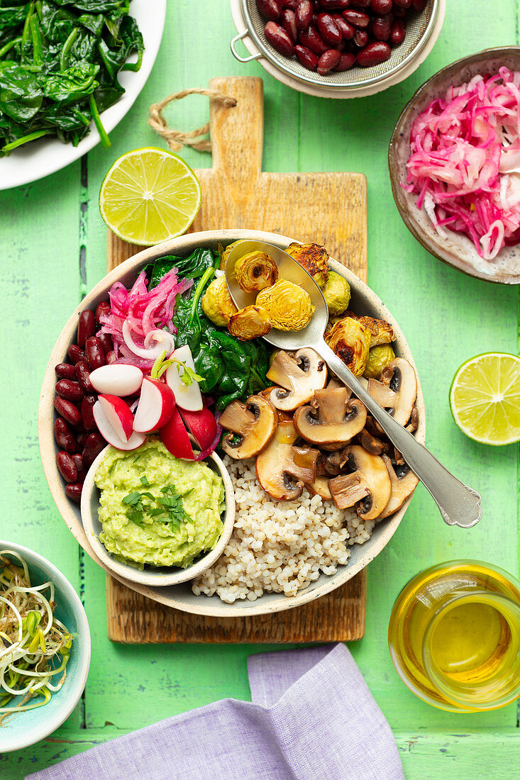 Buddha bowl (vegan) with spelt, mushrooms, brussel sprouts, spinach, red kidney beans and guacamole, marinated red onion