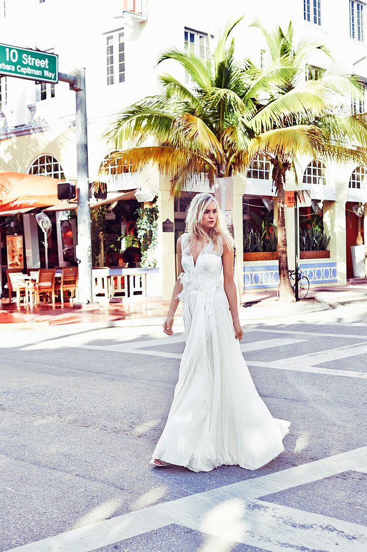 A young blonde woman wearing a white wedding dress outside on the street
