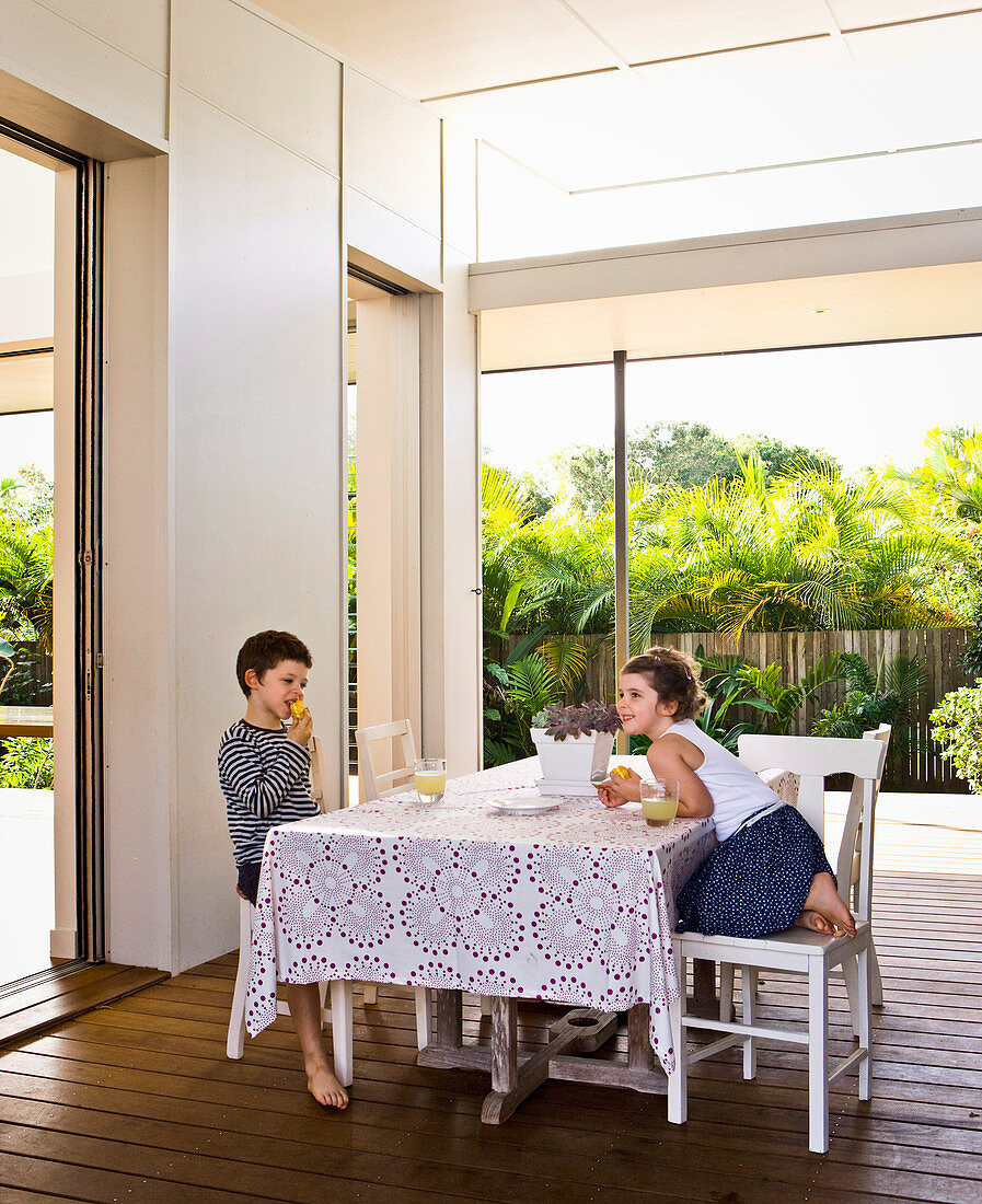 Girl and boy sit at the table on the veranda