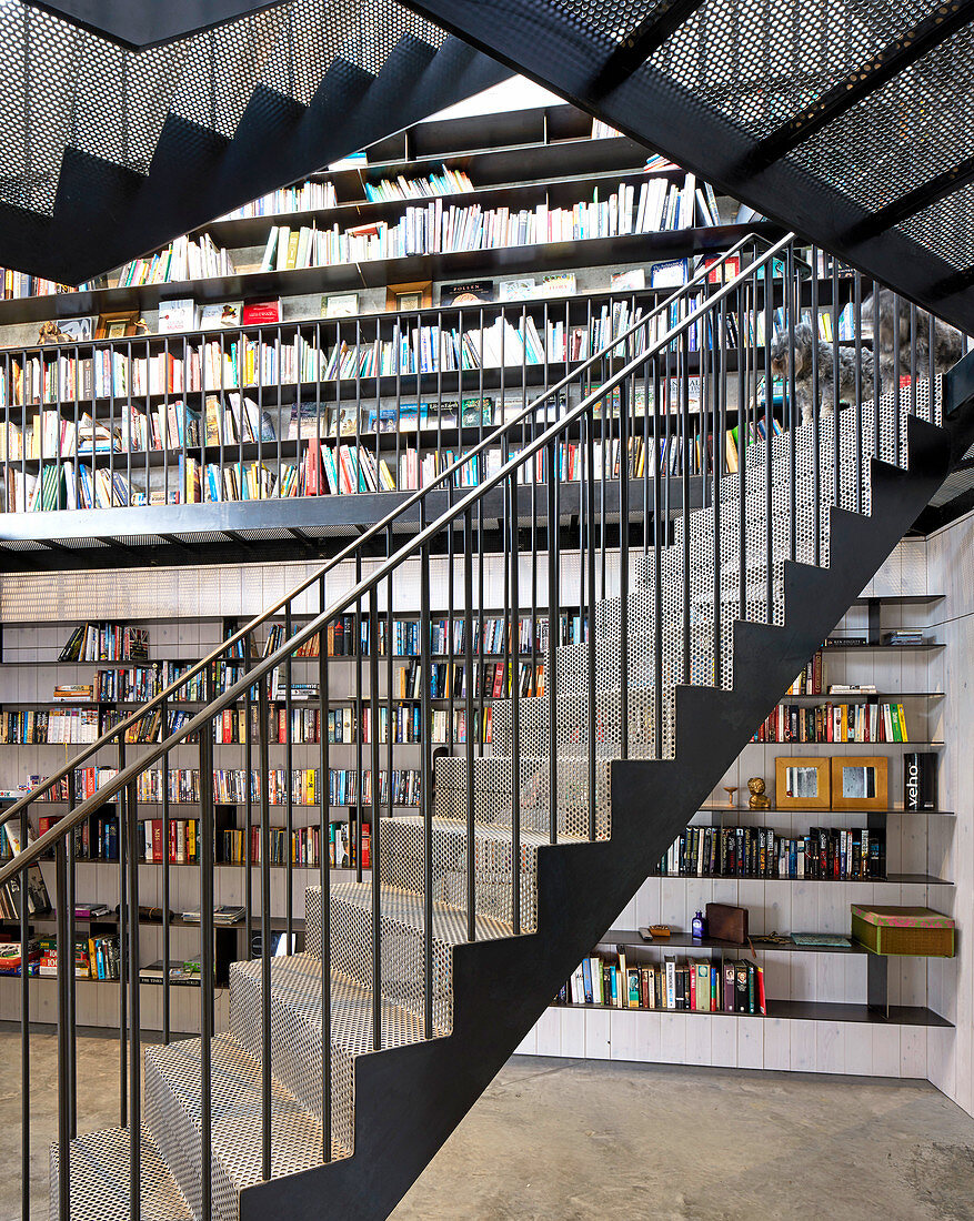 Freitragende Treppe aus Lochmetall vor Bücherwand