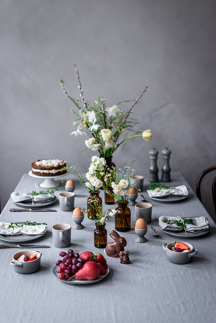 Gedeckter Tisch zum Osterfrühstück mit gekochten Eiern, Möhrentorte, Schokoladenhasen und Obstsalat