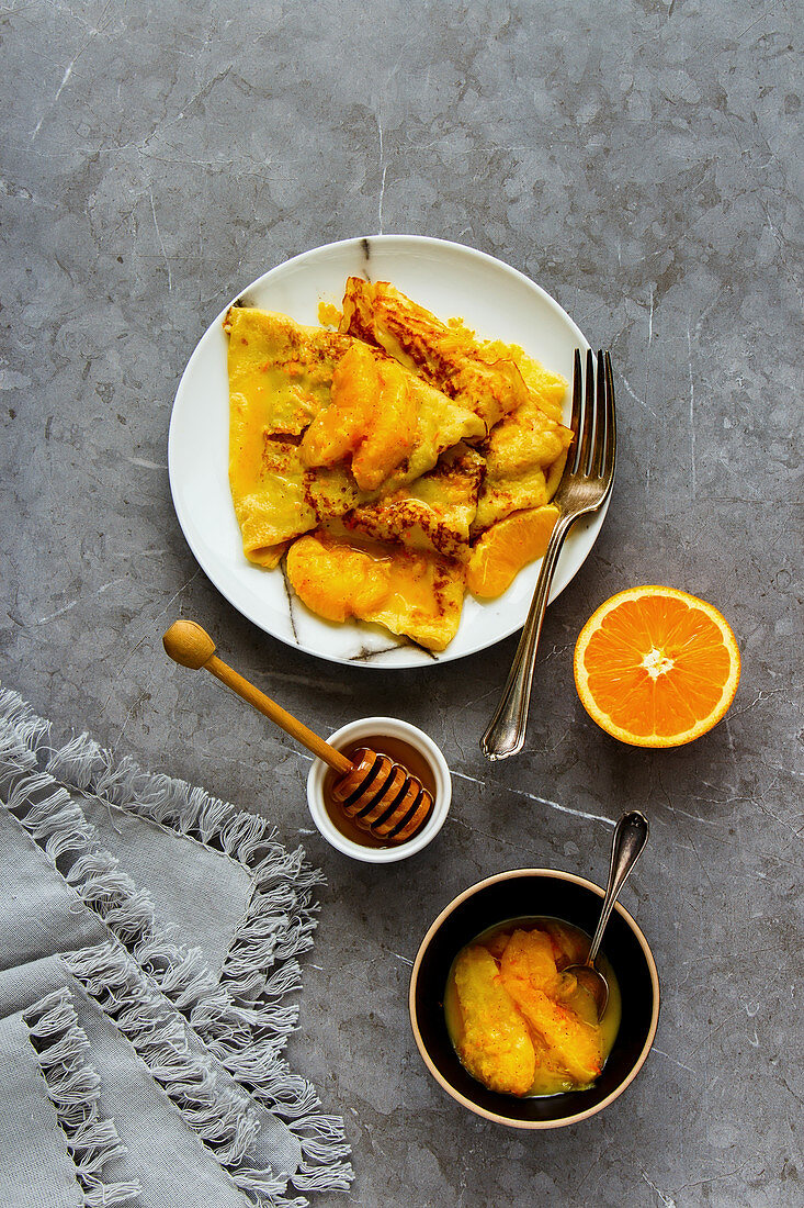 Crepes Suzette on plate flat lay. Thin pancakes with orange sauce over grey concrete table background
