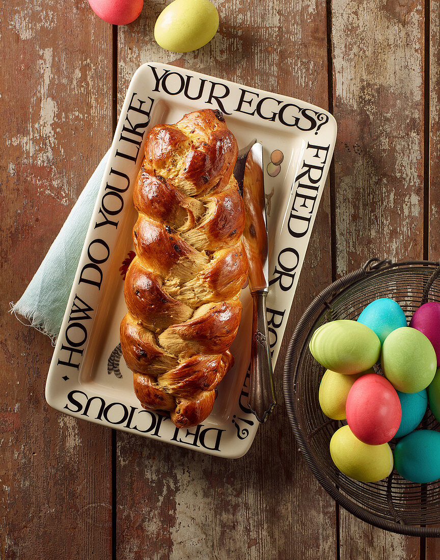 A glazed bread plait and coloured Easter eggs in a wire basket