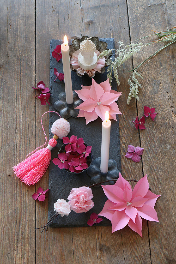 Tischdekoration mit Papierblumen und grauen Kerzen auf Schieferplatte