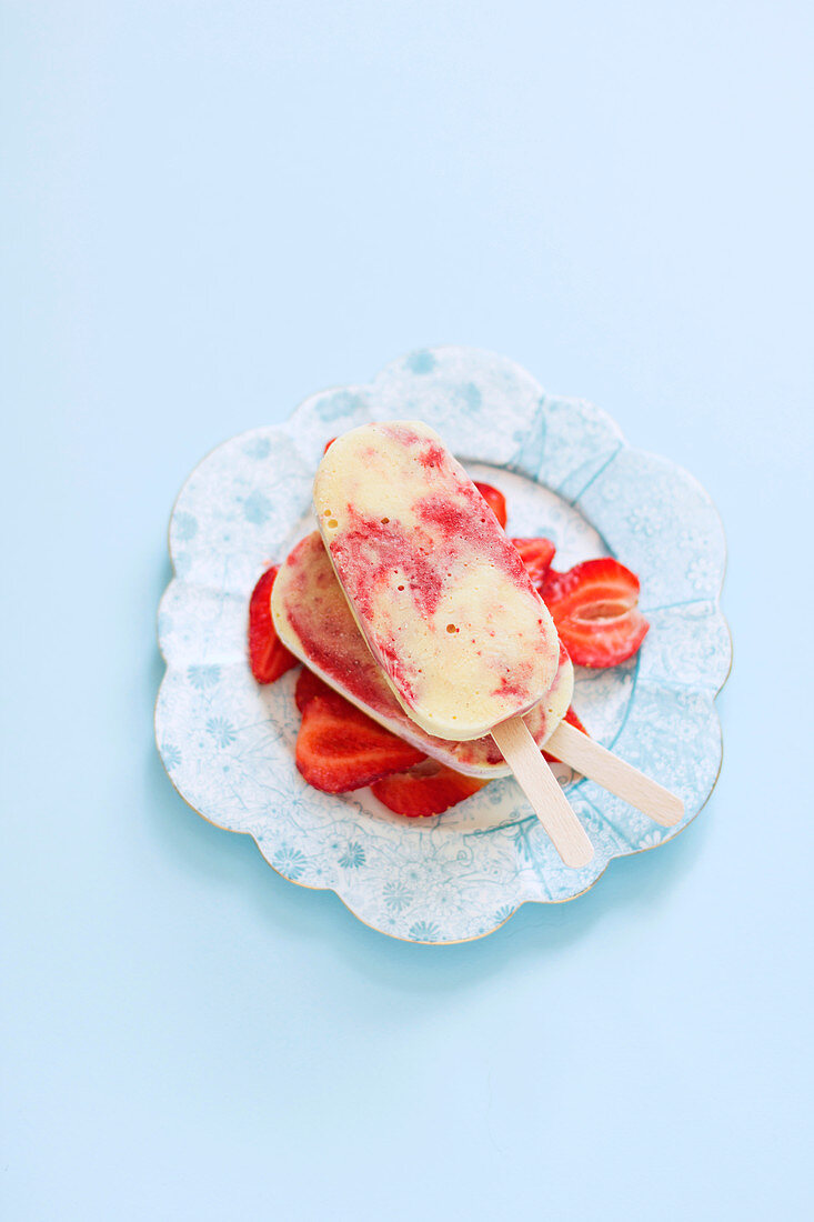 Two strawberry and custard popsicles on an old porcelain plate with strawberry slices