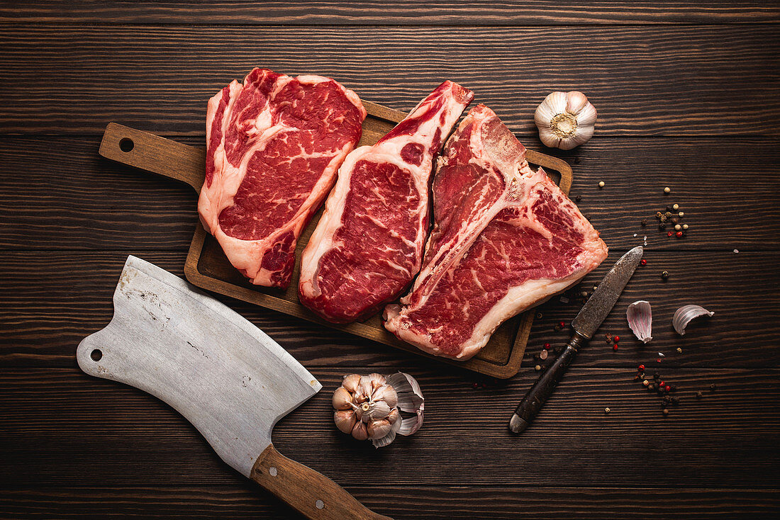 Raw rib-eye steak, a T-bone steak and a cowboy steak