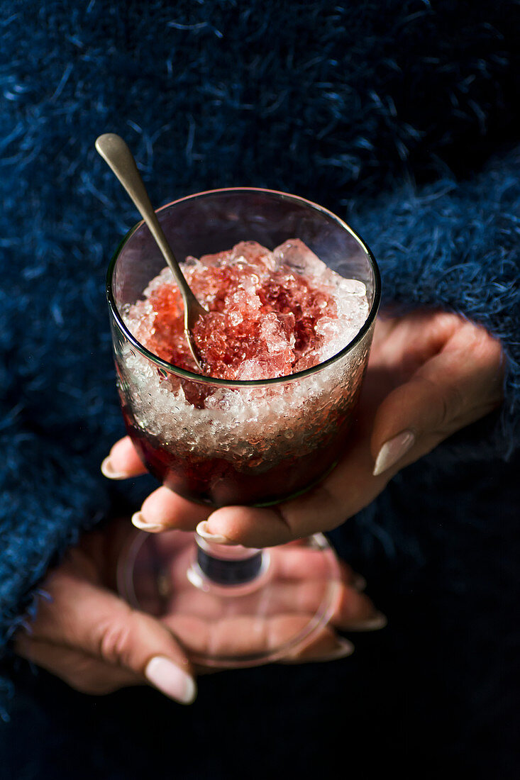 Frau hält ein Glas Crushed Ice mit Himbeersirup