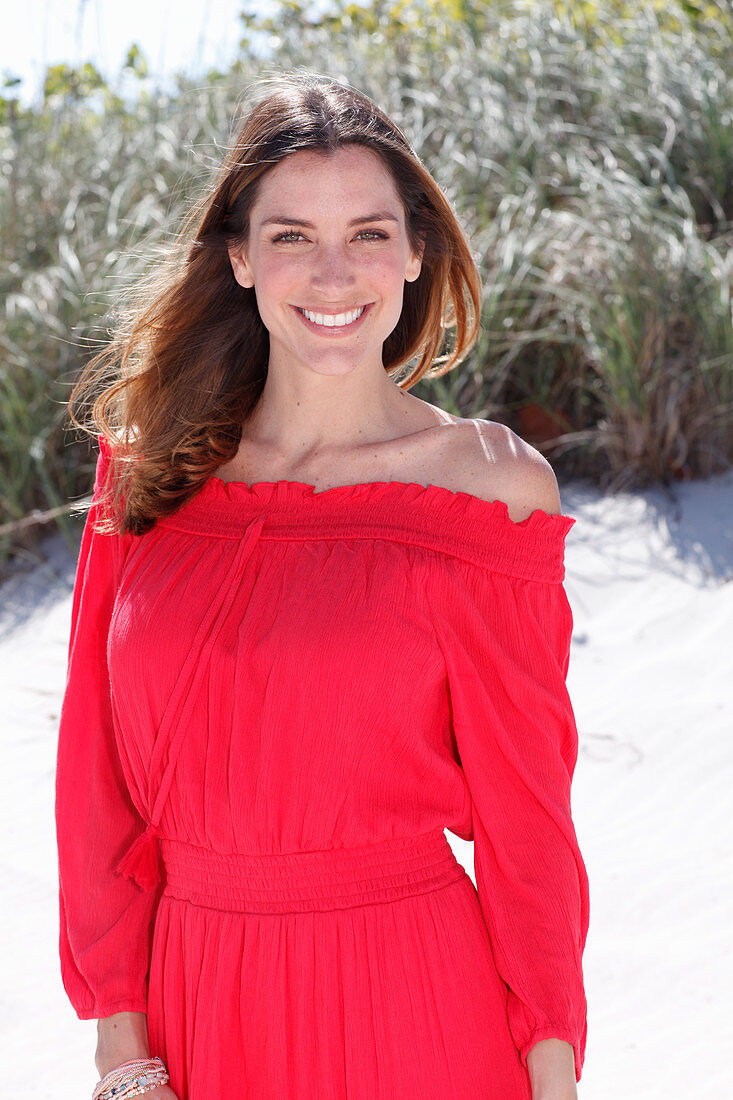 A brunette woman outside wearing a red off-the-shoulder dress