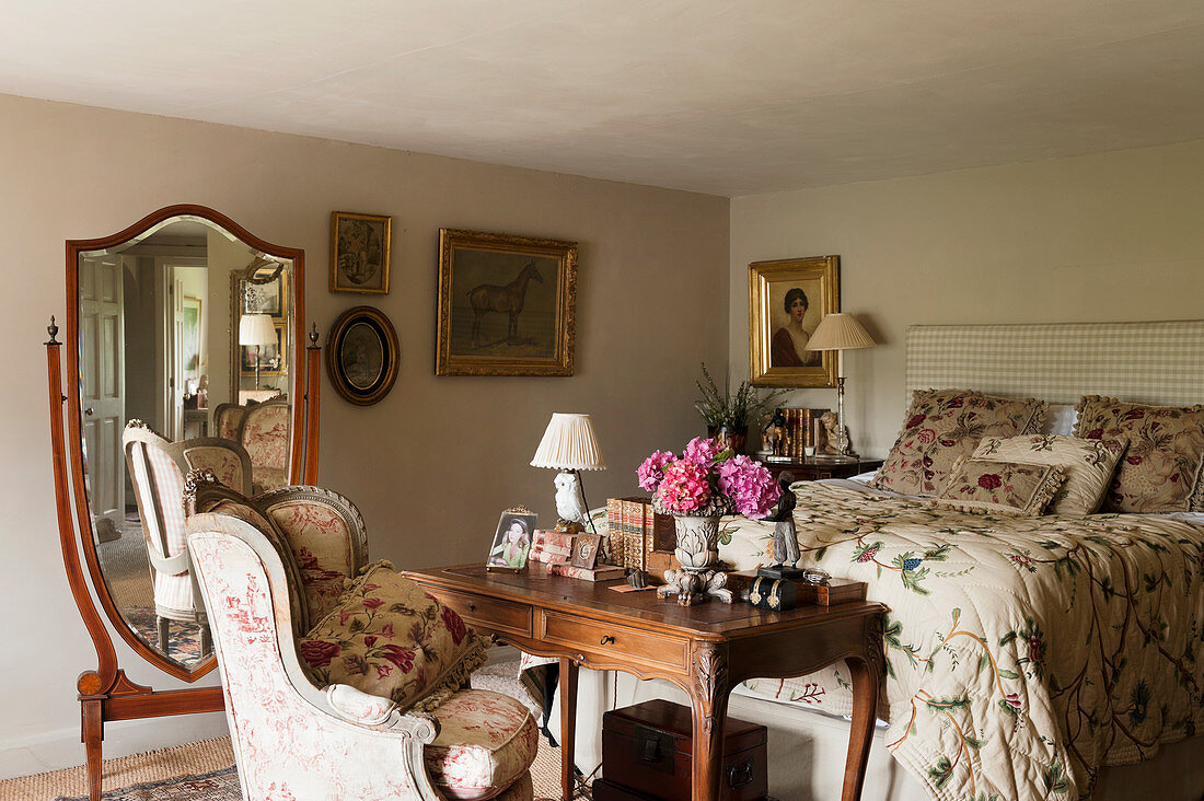 Antique cheval mirror, dressing table with armchair and bed with floral quilt in bedroom