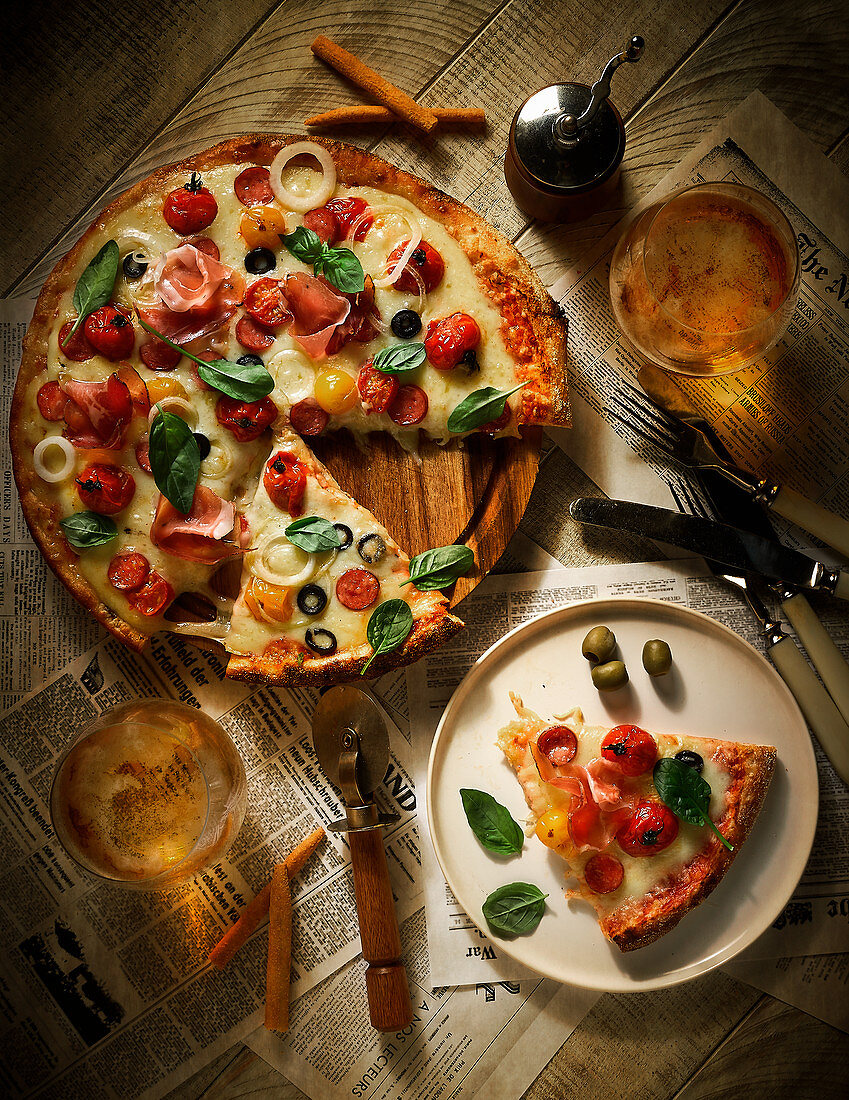 Pizza mit Salami, Schinken, Tomaten, Oliven und Käse auf Tisch