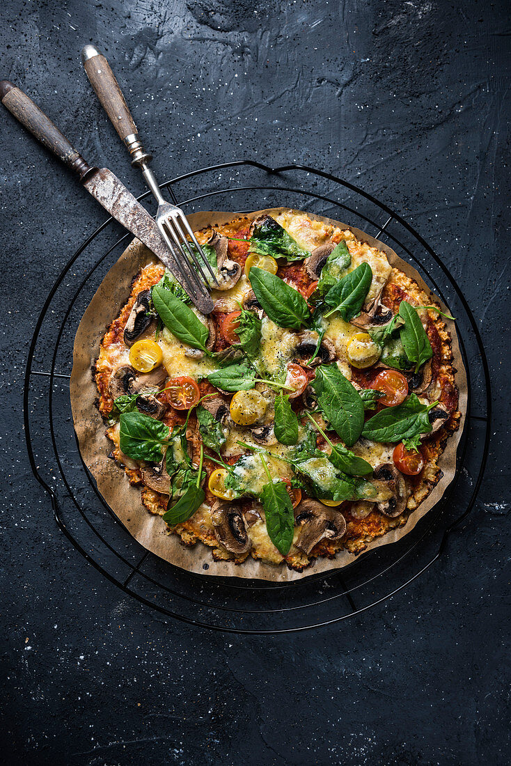 Gluten-free, vegan cauliflower pizza with tomatoes, mushrooms, spinach and cheese substitute