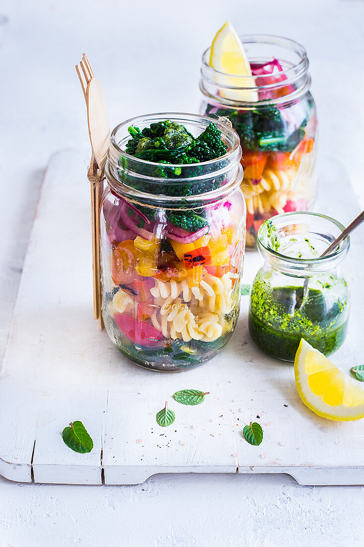 Pasta salad with kale and roasted vegetables in a jar, drizzled with kale pesto and a squeeze of lemon