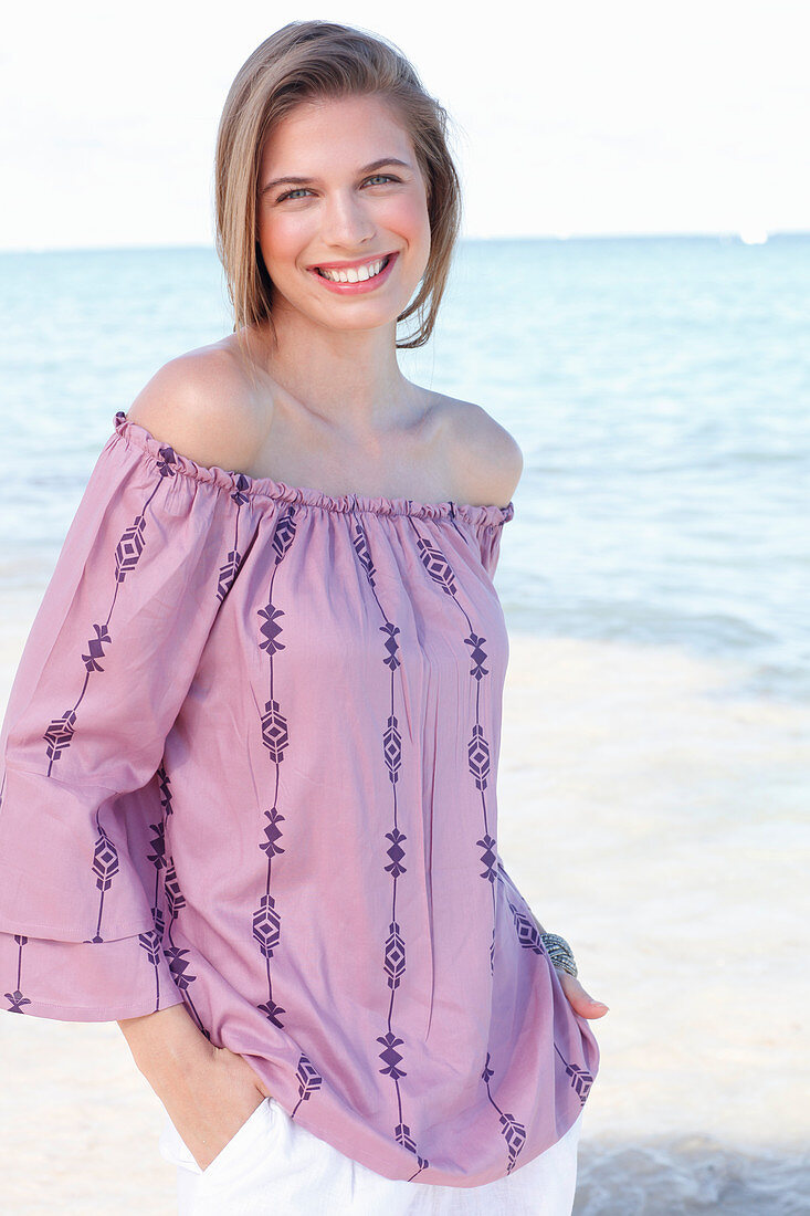 A young woman by the sea wearing a Carmen blouse