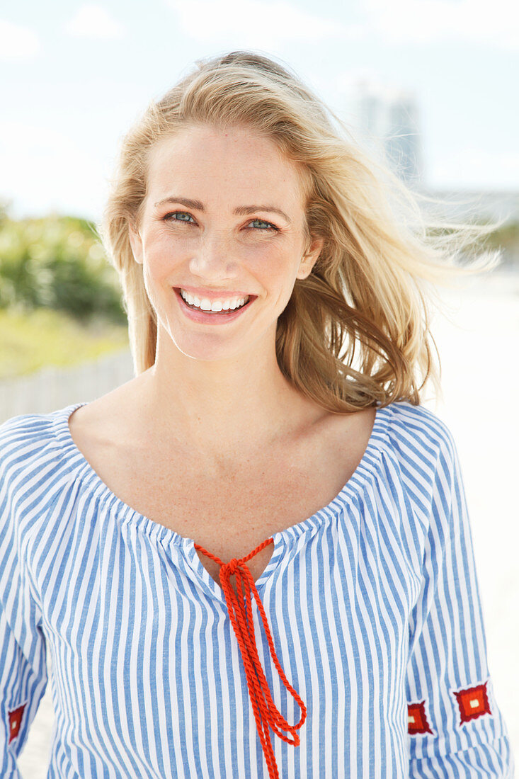 A blonde woman outside wearing a blue-and-white striped blouse