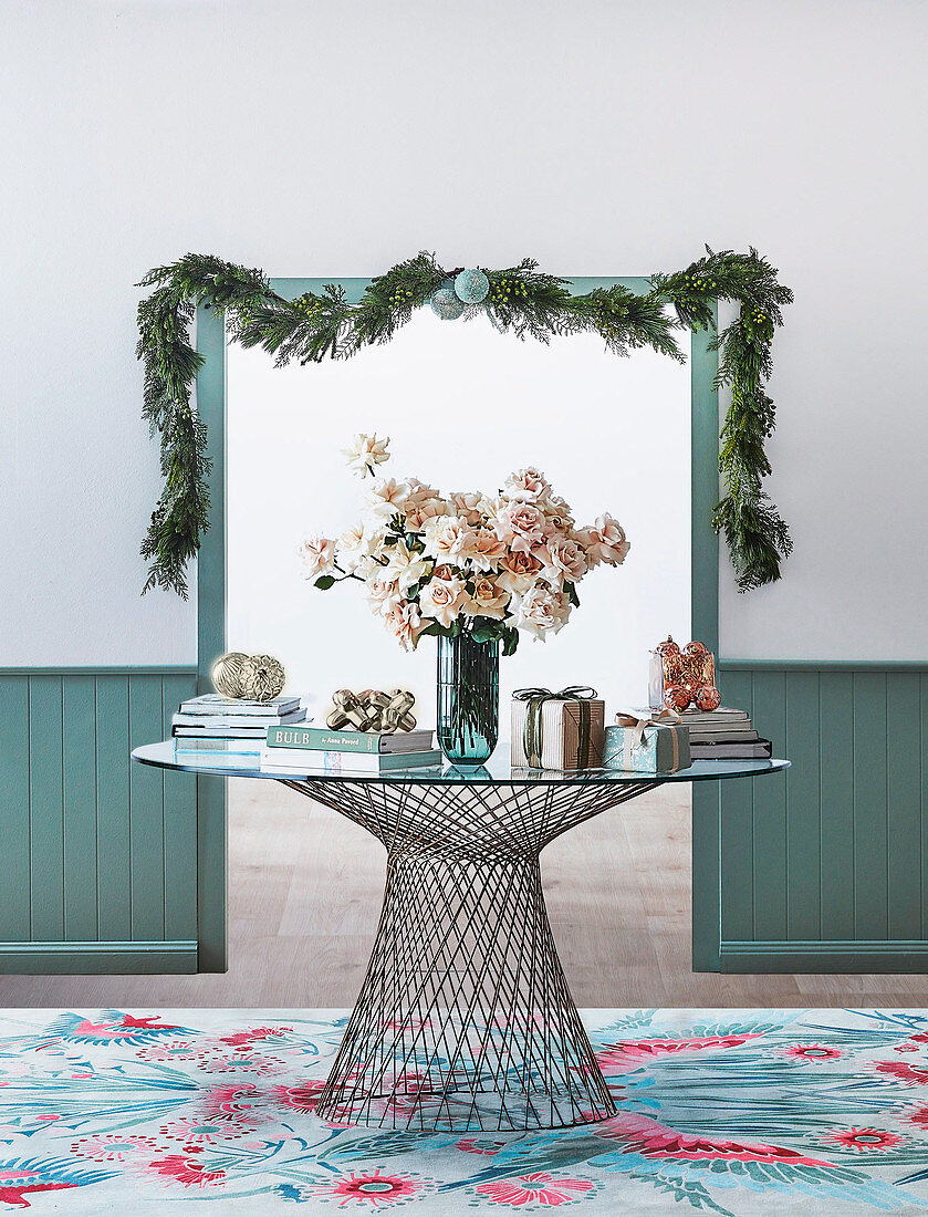 Round metal and glass table with bouquet and gifts in front of passage with Christmas garland