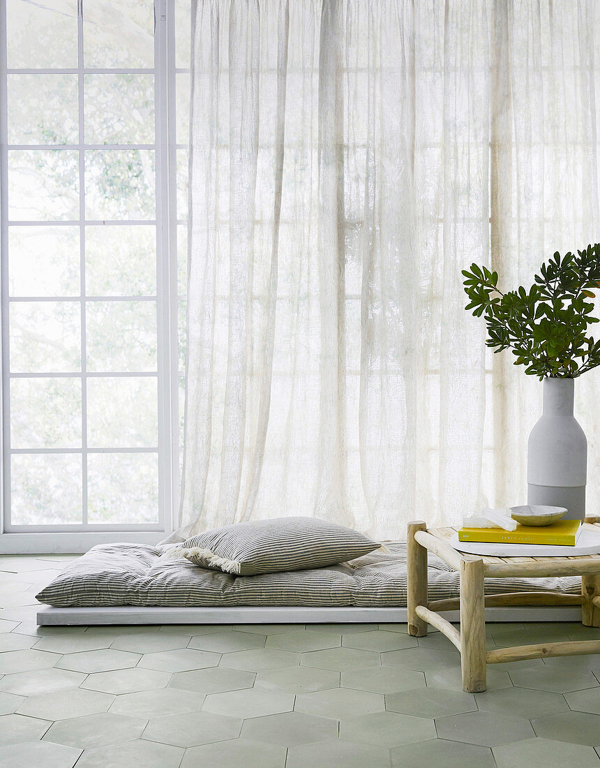 Floor mat with pillows in front of a window next to a side table with a vase