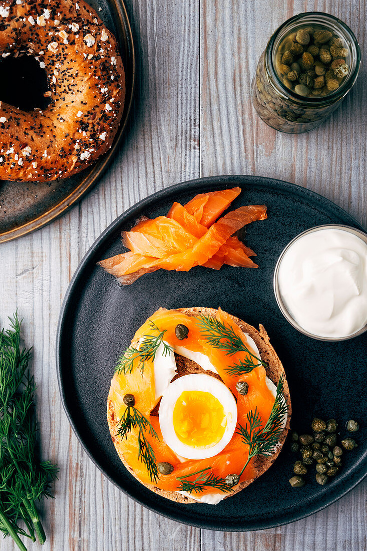 Mehrkorn-Bagel mit Räucherlachs, Creme Fraiche, Ei, Kapern und Dill