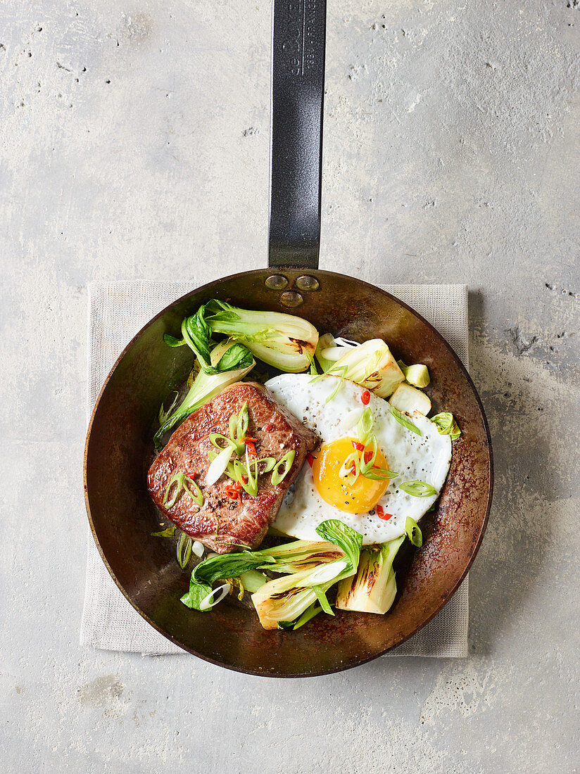 A steak pan with bok choy and a fried egg