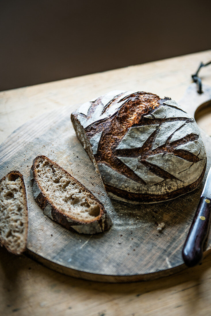 Ein Sauerteigbrot mit Ährenmuster, angeschnitten auf Holzbrett