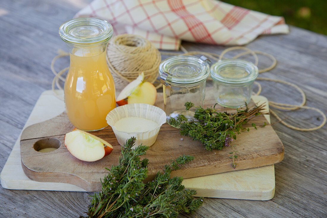 Ingredients and glass jars for thyme jelly with apple juice on a wooden table