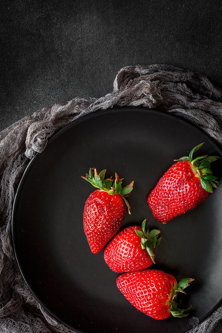 Red and fresh strawberries flat lay in black dish