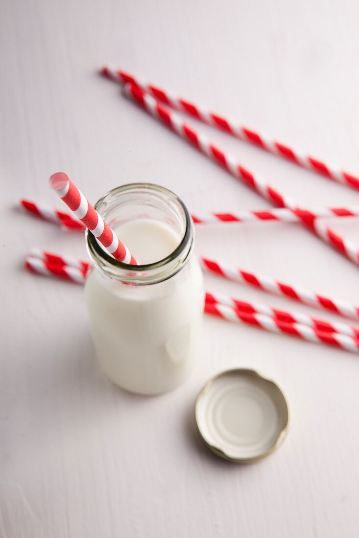 A small bottle of milk and several red and white straws