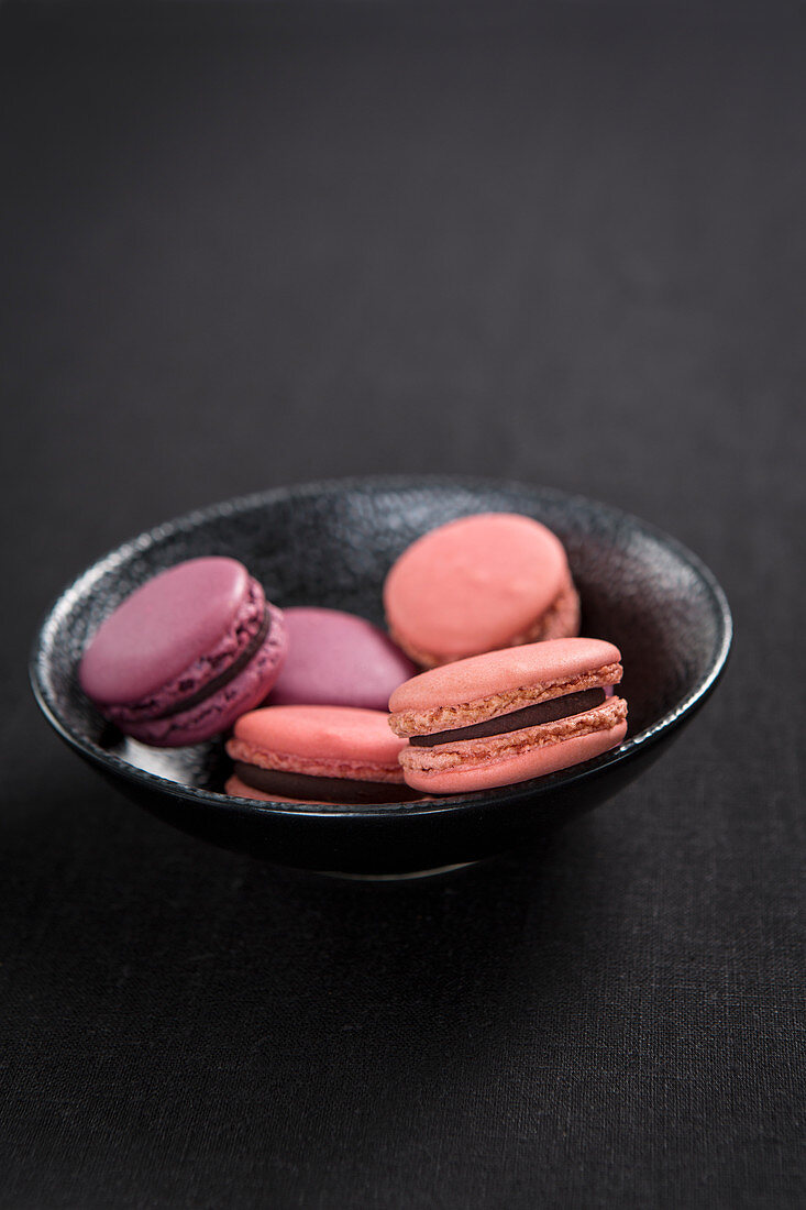 Verschiedene rosafarbene Macarons in schwarzem Schälchen