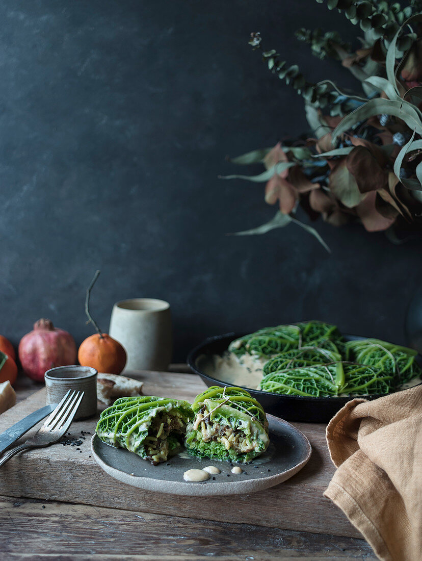 Cabbage leaves stuffed with rice on plate near pan, slice of bread and fork on wooden background