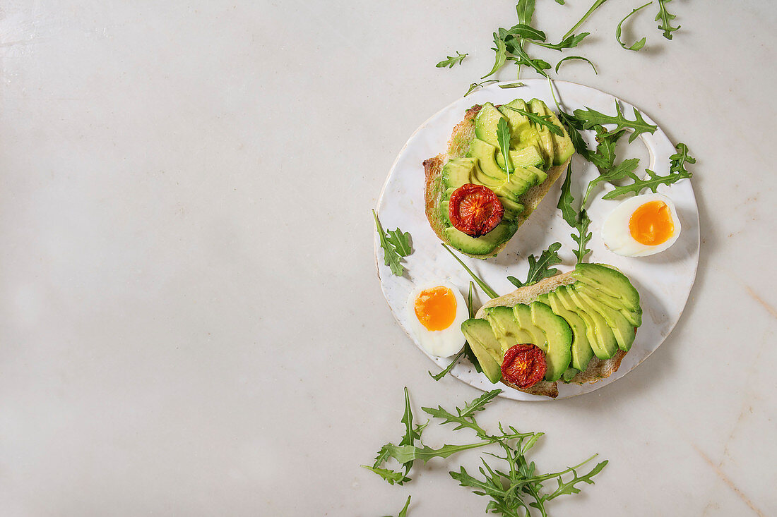 Belegtes Brot mit Avocado, getrockneten Tomaten, Ei und Rucola