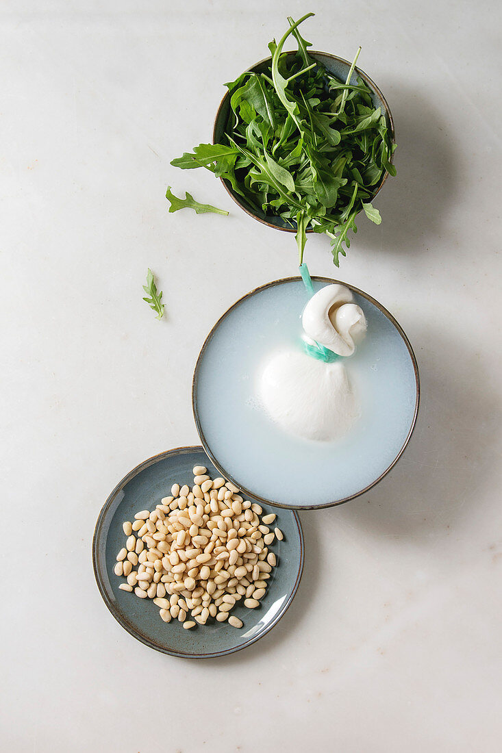 Bowl with whole tied Italian cheese burrata in brine, arugula salad and pine nuts