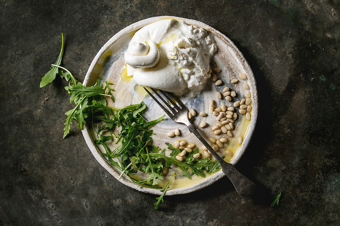 Burrata-Käse mit Olivenöl, Pinienkernen und Rucola (Italien)