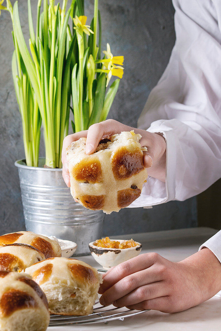 Child hands take homemade Easter traditional hot cross buns on cooling rack on white marble table