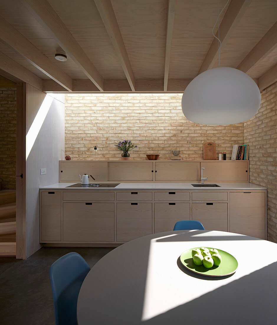 Round table in open-plan modern kitchen with counter, brick wall and skylight