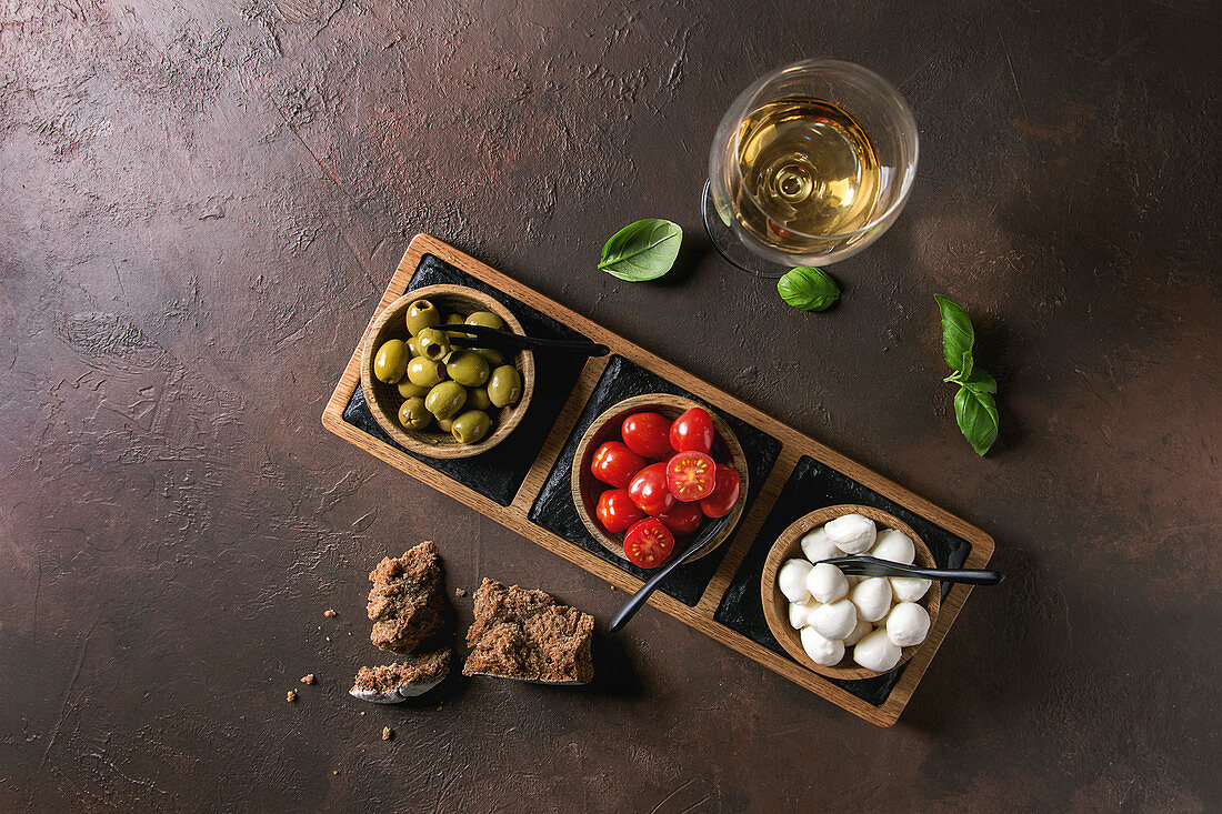 Mozzarella, Kirschtomaten und Oliven als Antipasti in Holzschälchen