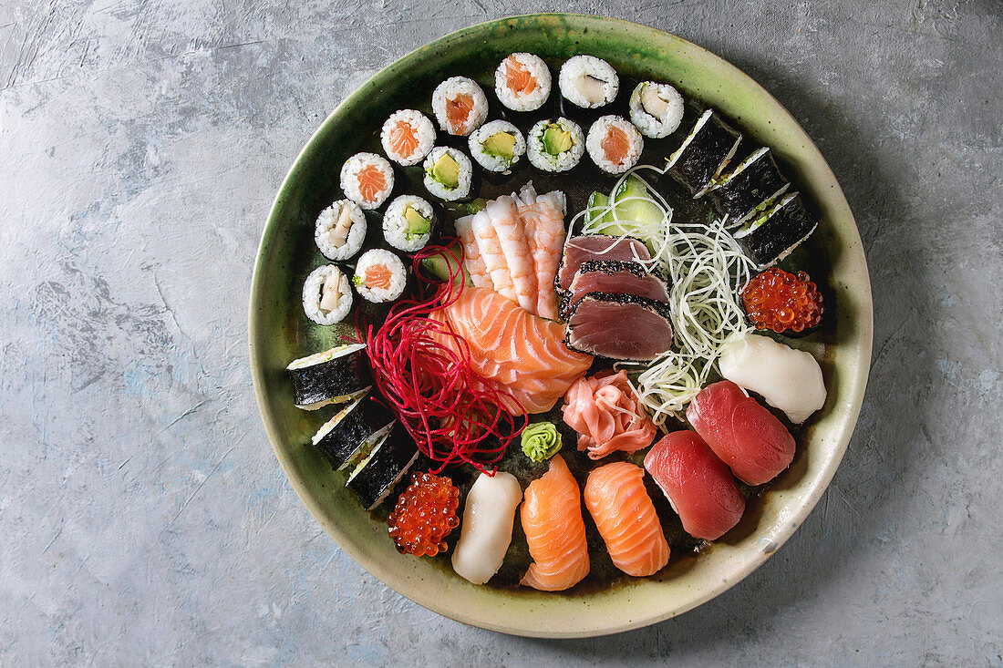 Sushi Set: nigiri, sashimi and sushi rolls in ceramic serving plate with salad