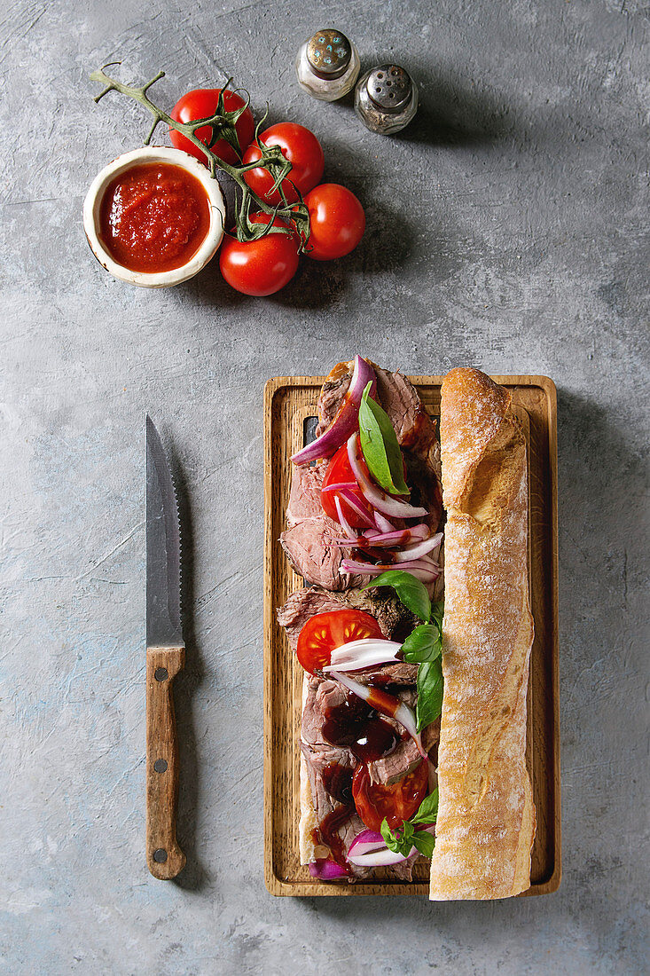 Beef baguette sandwich with tomatoes, basil and red onion