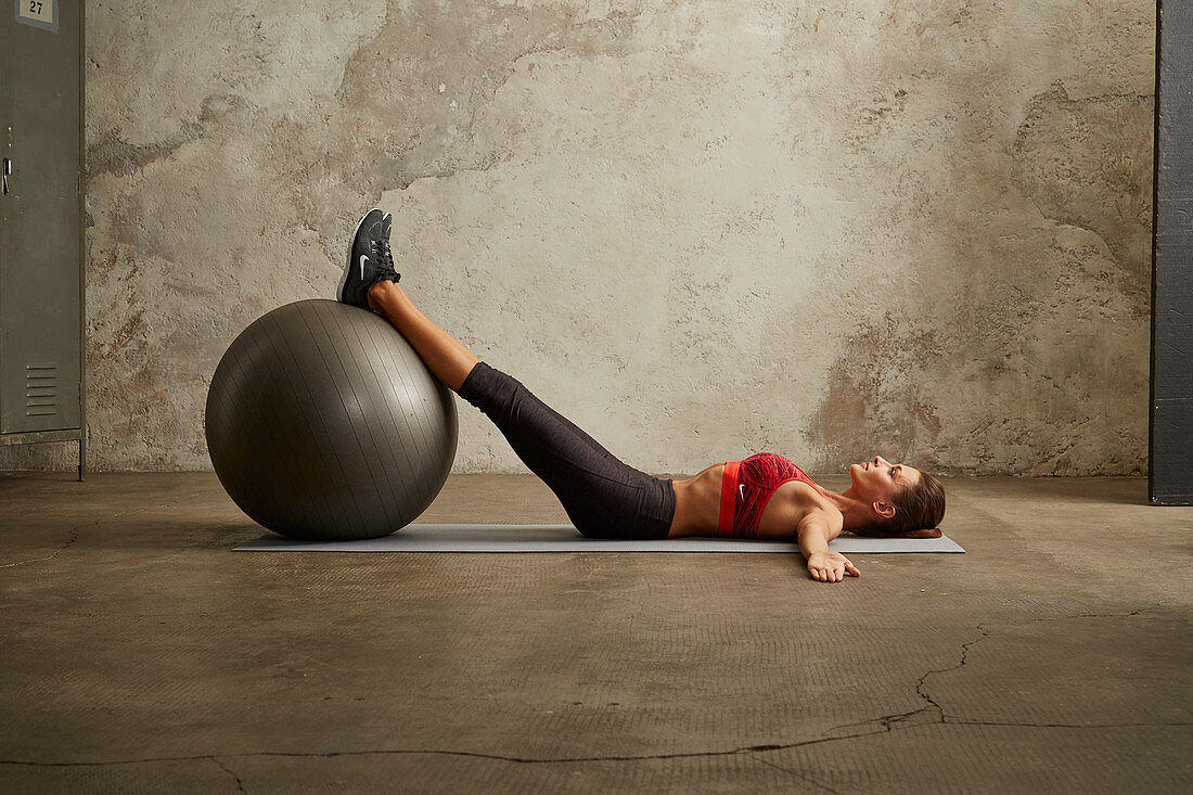 A young woman lying on her back with her legs on a gym ball