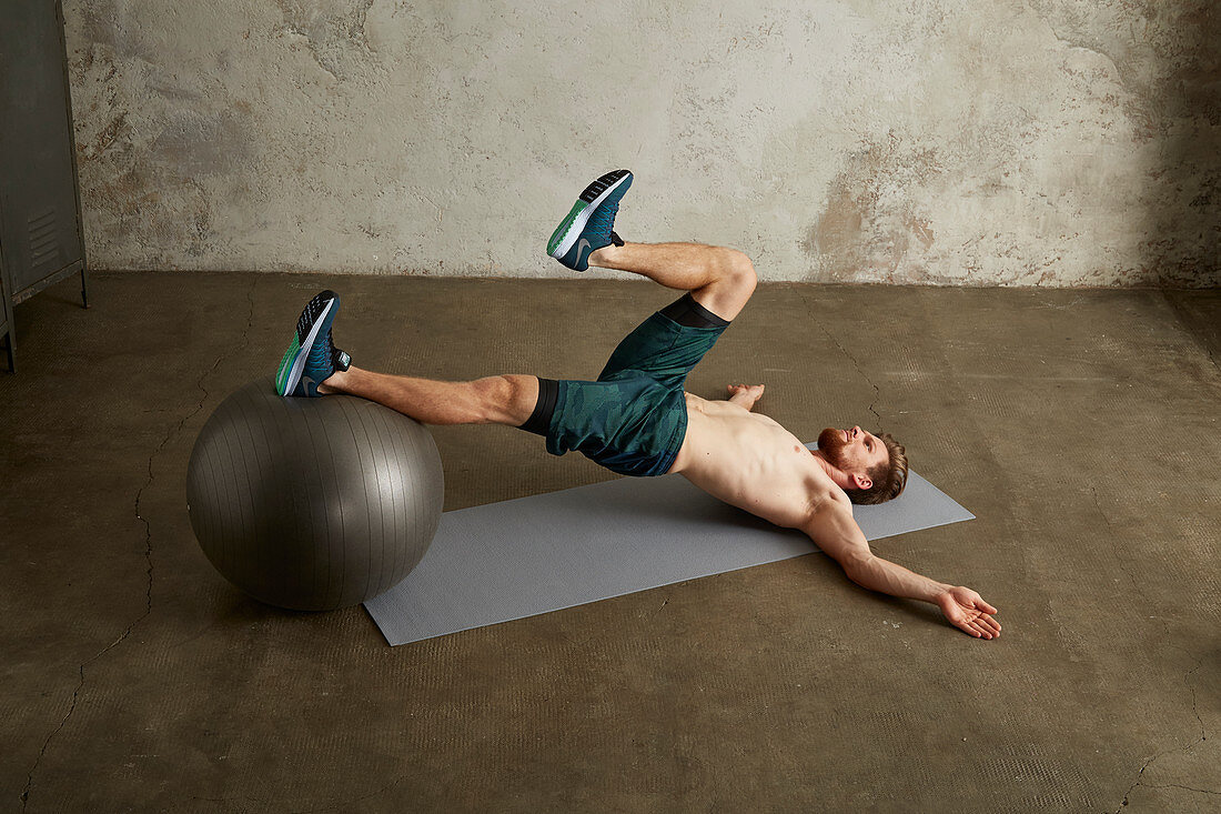 A young man lying on his back with one foot on a gym ball and one leg bent up
