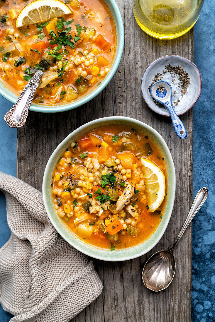 Two bowls of chicken and vegetable soup on a rustic board