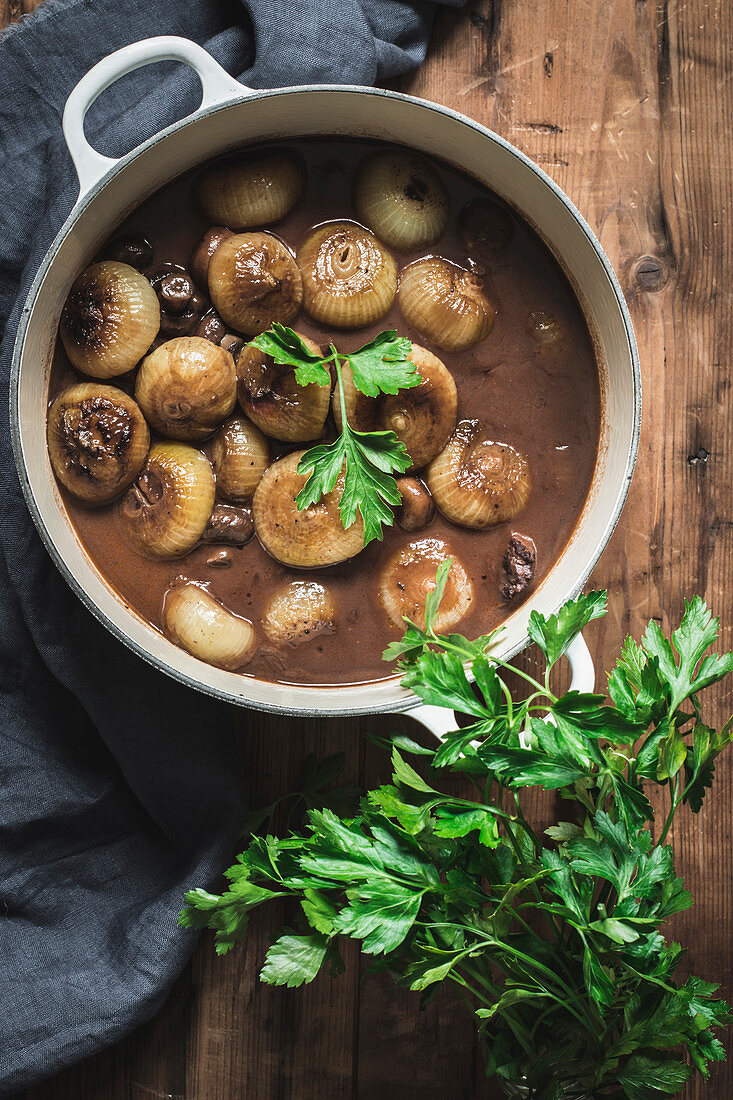 Cooking pot with Boeuf Bourgingnon with mushrooms and green herbs on wooden table