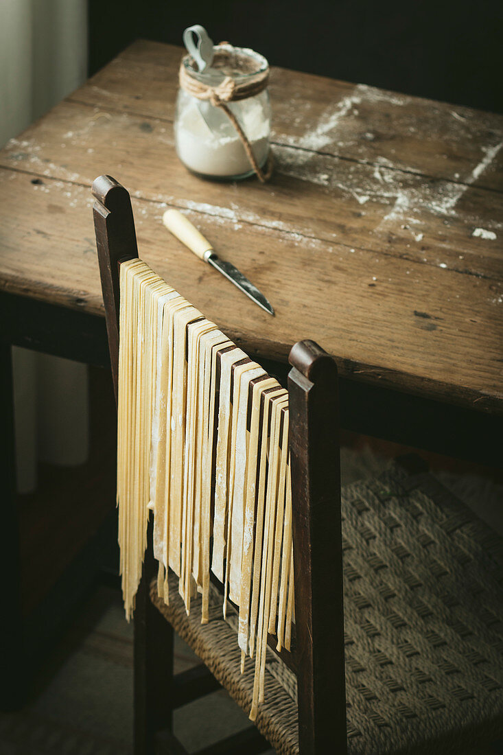 Frische selbstgemachte Bandnudeln hängen zum Trocknen auf Holzstuhl